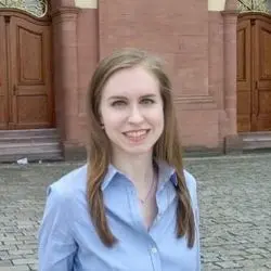 Julia Werling in hellblauer Bluse und mit langen bloden Haaren auf dem Ehrenhof