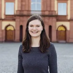 Regina Gau mit schulterlangen braunen Haaren in einem grauen Oberteil auf dem Ehrenhof