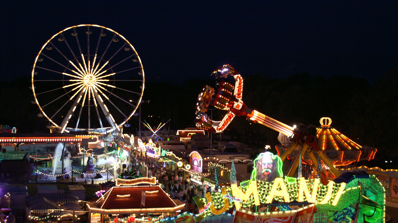 Die bunten Lichter eines Riesenrades und einiger Fahrgeschäfte leuchten in der Nacht.