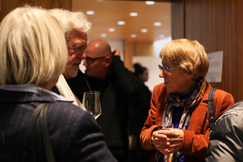 Einige Personen stehen winterlich mit Jacken und Anzügen bekleidet mit Gläsern in den Händen in einem holzvertäfelten Ambiente. Identifizierbar ist Prof. Dr. Ursula Wolf im Gespräch.