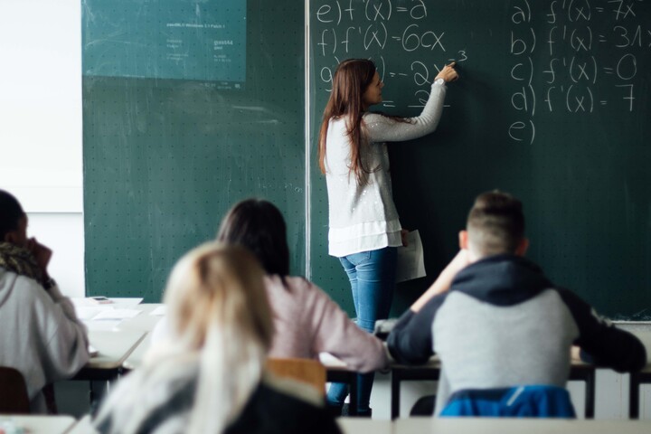 Eine Dozentin schreibt mathematische Formeln an eine Kreidetafel
