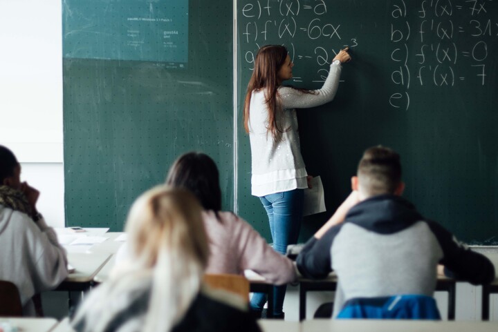 Eine Dozentin schreibt mathematische Formeln an eine Kreidetafel