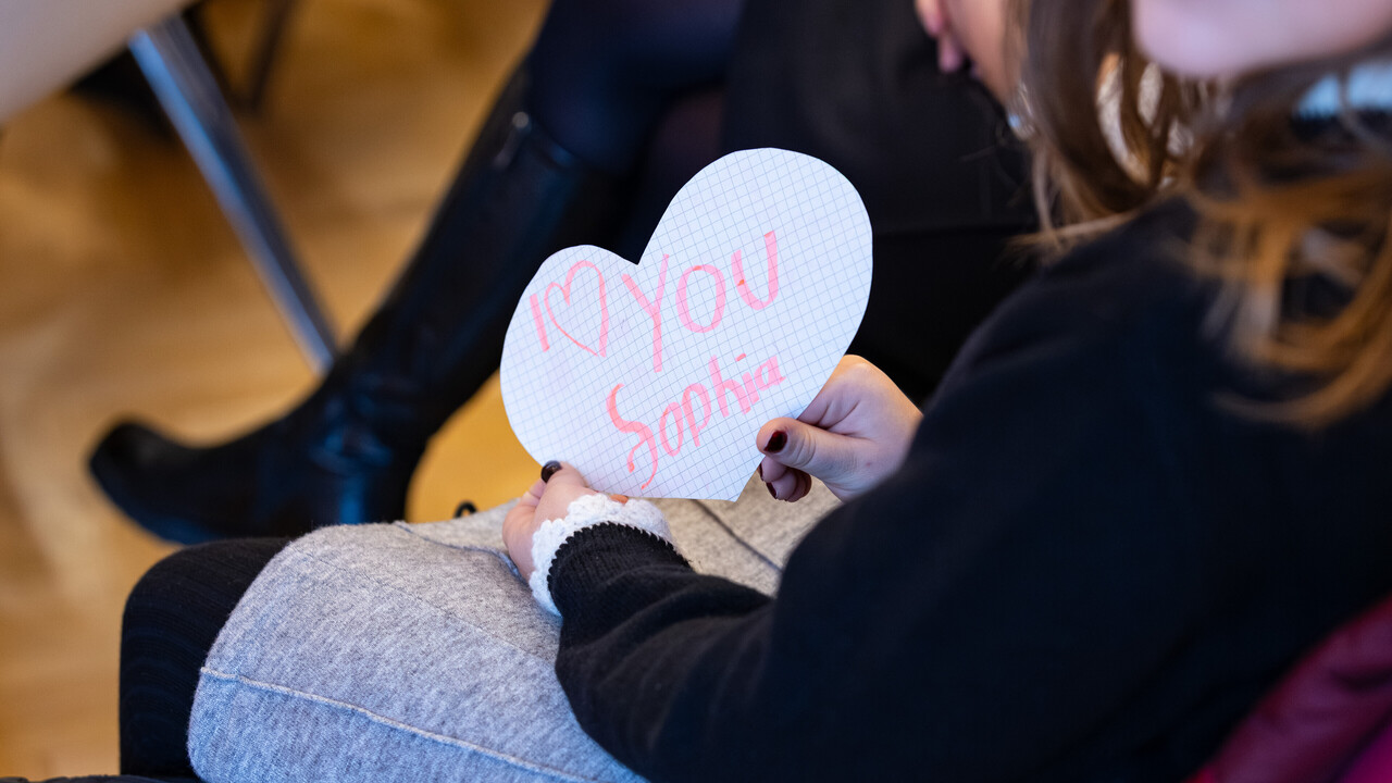 In Mädchen hält ein Herz mit der Aufschrift "I love you Sophia" in die Kamera.