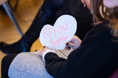 In Mädchen hält ein Herz mit der Aufschrift "I love you Sophia" in die Kamera.