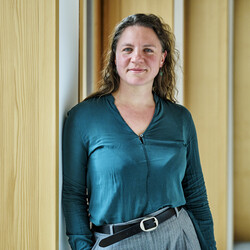 Eine Frau lehnt sich seitlich mit ihrer Schulter gegen eine Wand und schaut in die Kamera.