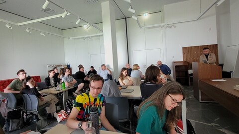 Die Teilnehmenden der Summer School sitzen in einem modernen Konferenzraum und hören dem Vortrag zu, einige machen sich Notizen.