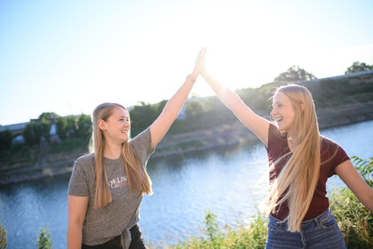 Zwei Studentinnen stehen am Neckarkanal und klatschen sich mit High-Five ab. Sie lachen und sind fröhlich.