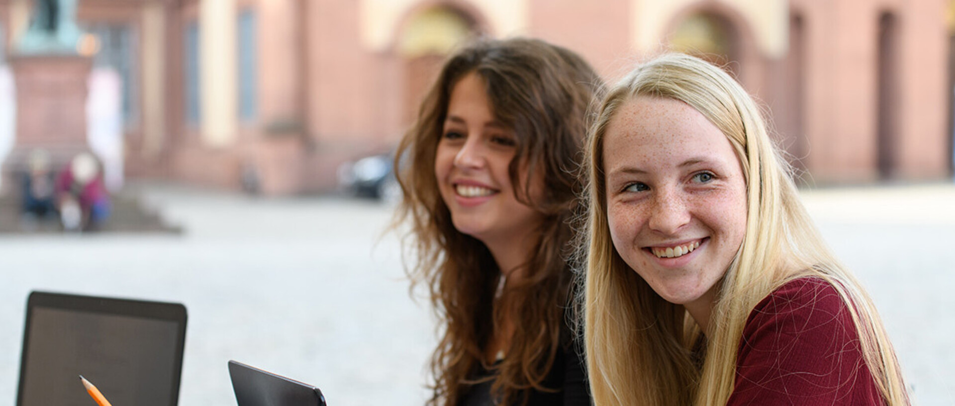 Zwei Studentinnen sitzen lachend vor dem Mannheimer Schloss.