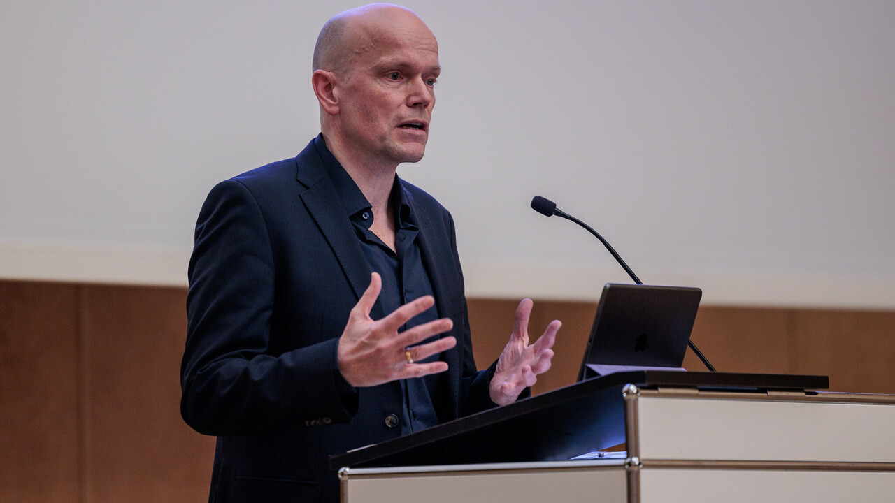 Vortrag durch Prof. Dr. Dietmar Heidemann Prof. Dr. Dietmar Heidemann am Rednerpult beim Vortrag zum Tag der Philosophie am 21.11.2024. Er trägt ein dunkles Jackett auf dunklem Hemd.