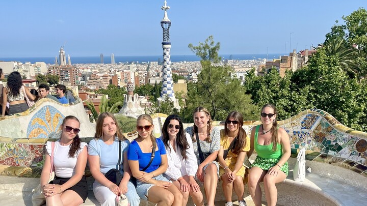 Gruppe Studierender mit Katalanischlektorin im Parc Güell. Im Hintergrund ist die Stadt Barcelona zu sehen. 