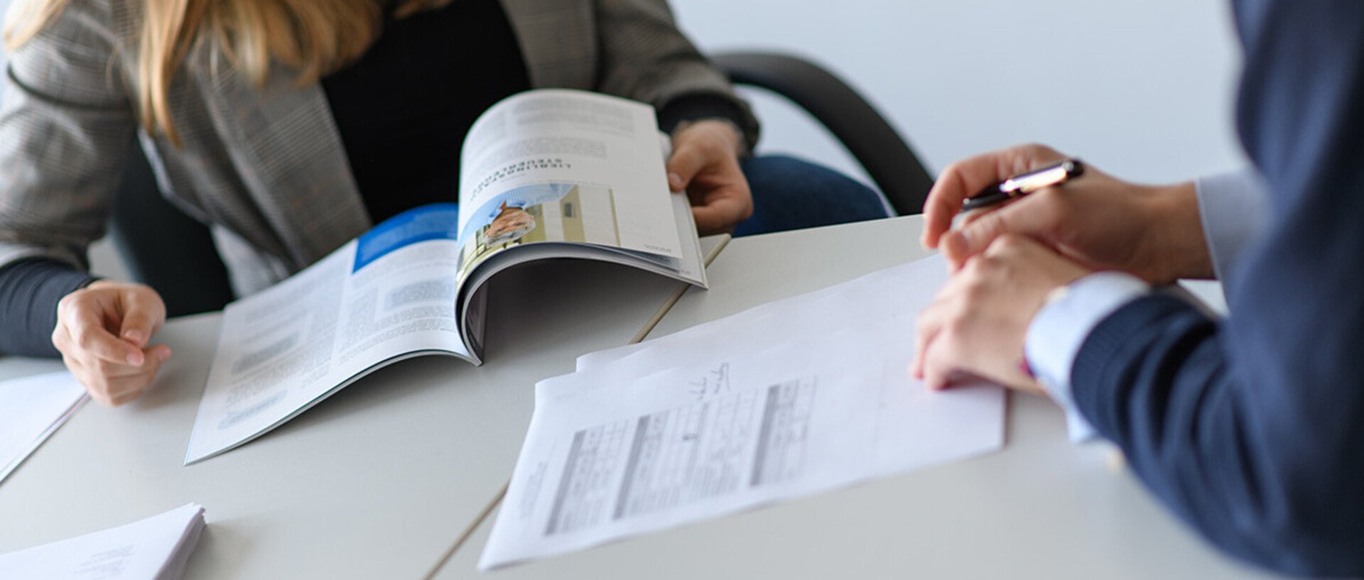 Zwei Menschen blättern in Dokumenten auf einem Tisch.