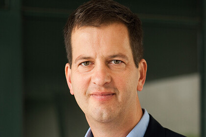 Philipp Lepenies trägt ein hellblaues Hemd und eine schwarze Anzugjacke. Das Hemd ist am Kragen geöffnet, die Jacke ist offen. Er hat kurzes, braunes Haar und zeigt ein angedeutetes Lächeln. 