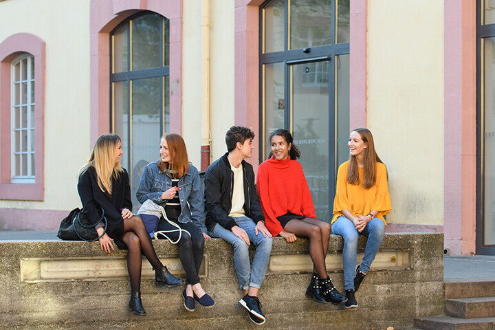 Fünf Studierende sitzen auf einer Mauer vor der Schneckenhof-Bibliothek.
