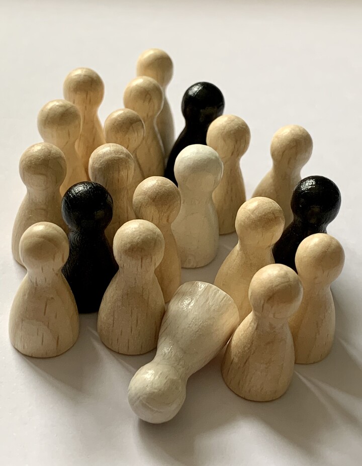 Etwa 20 kegelförmige Spielfiguren in drei Farben (Braun, Weiß und Schwarz) stehen scheinbar ohne Ordnung in einer Gruppe zusammen; eine Figur liegt auf der Seite. 