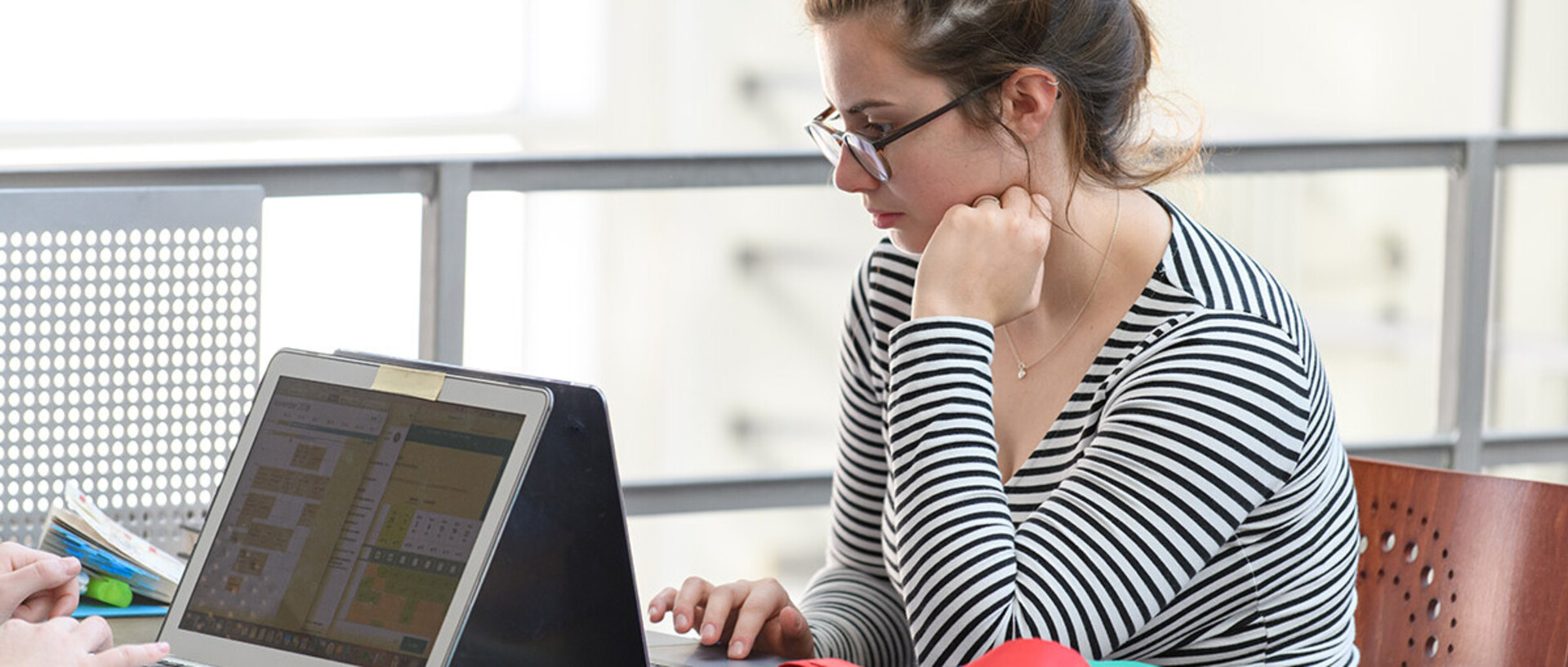 Studentin mit Brille arbeitet am Laptop in der Bibliothek.