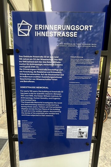 Eine Infotafel vor dem Gebäude des Erinnerungsort Ihnenstraße. Darauf steht: "Das Gebäude Ihnestraße 22 ist seit rund 100 Jahren ein Ort der Wissenschaft: Von 1927 bis 1945 befand sich hier das Kaiser -Wilhelm-Institut für Anthropologie, menschliche Erblehre und Eugenik (KWI-A). Der Erinnerungsort Ihnestraße beschäftigt sich mit Forschung, die Rassismus und Entmensch-lichung hervorbrachte. Auf vier Stockwerken und im Außenraum erzählen Austellungsstationen Geschichten von Wissenschaftler*innen und Betroffenen."