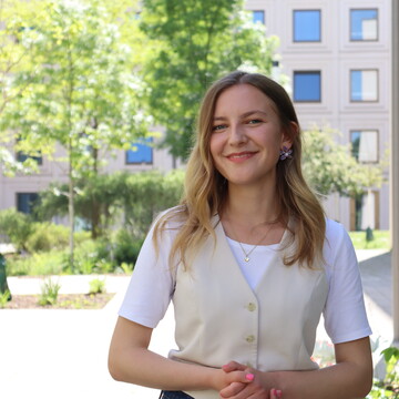 Sophia Kriesch im Außenbereich bei B6. Sie hat schulterlange blonde Haare und trägt eine weiße Weste.