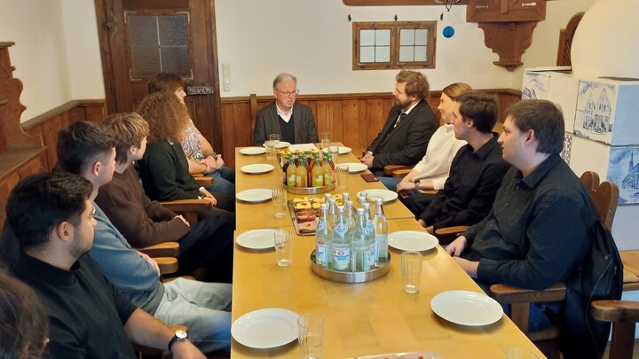 Mehrere Personen an einem gedeckten Tisch in einer alten Stube