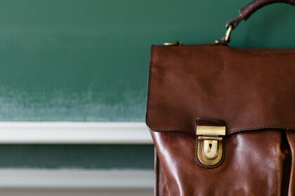 Eine braune Ledertasche steht im Vordergrund einer Kreidetafel