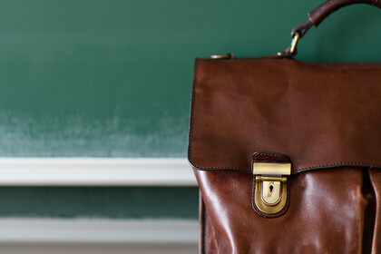 Eine braune Ledertasche steht im Vordergrund einer Kreidetafel