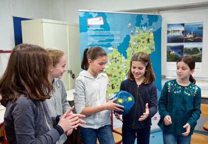 Fünf Kinder reichen sich gegenseitig einen blauen Würfel. Im Hintergrund, eine Karte von Frankreich und Deutschland.