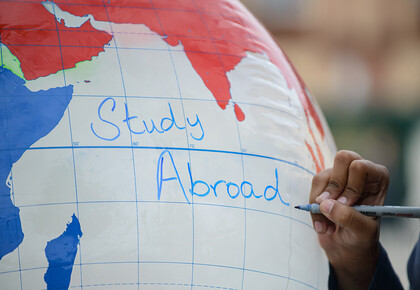 Jemand schreibt mit einem Stift auf eine Weltkugel "Study abroad".