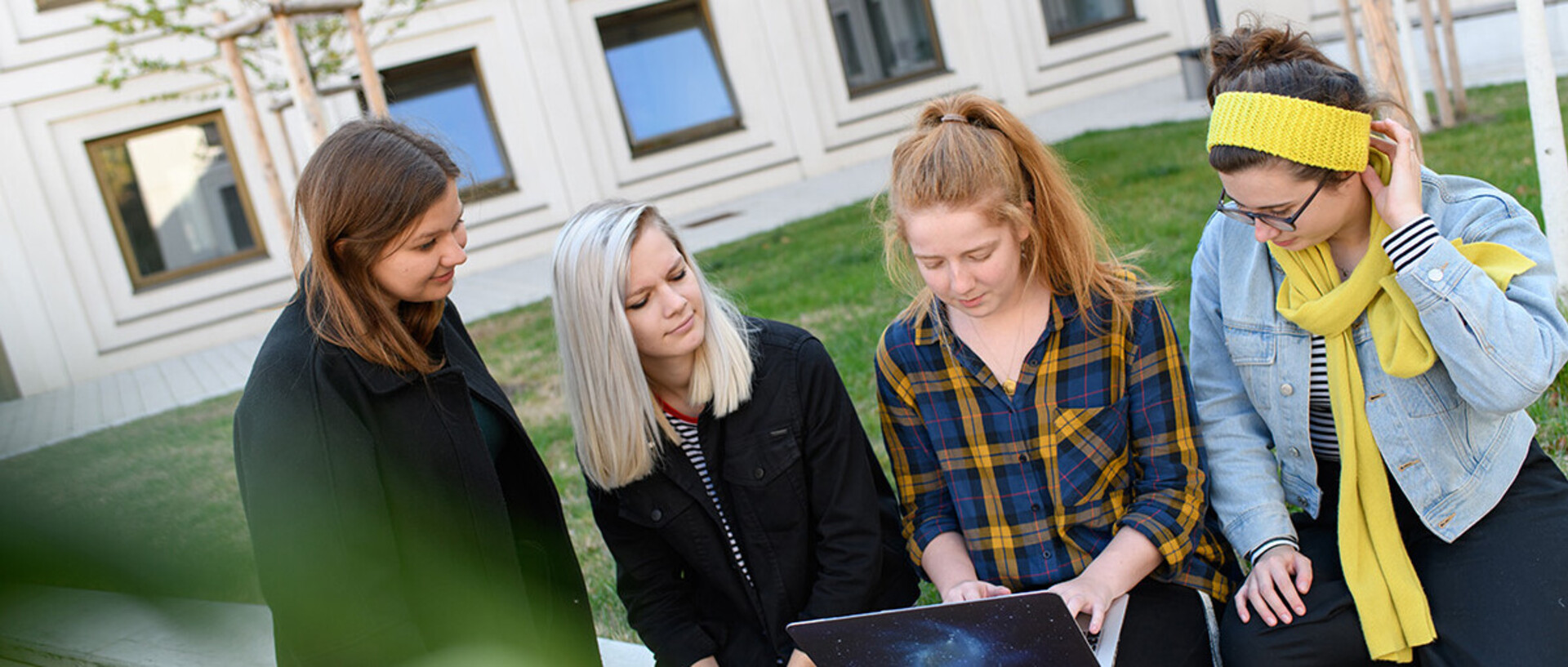 Studentinnen mit Laptop auf Wiese in einem Innenhof.