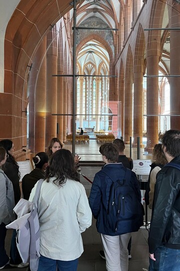 Eine Gruppe von Personen im Eingang der gotischen Heidelberger Stiftskirche, die einer anderen Person zuhören.