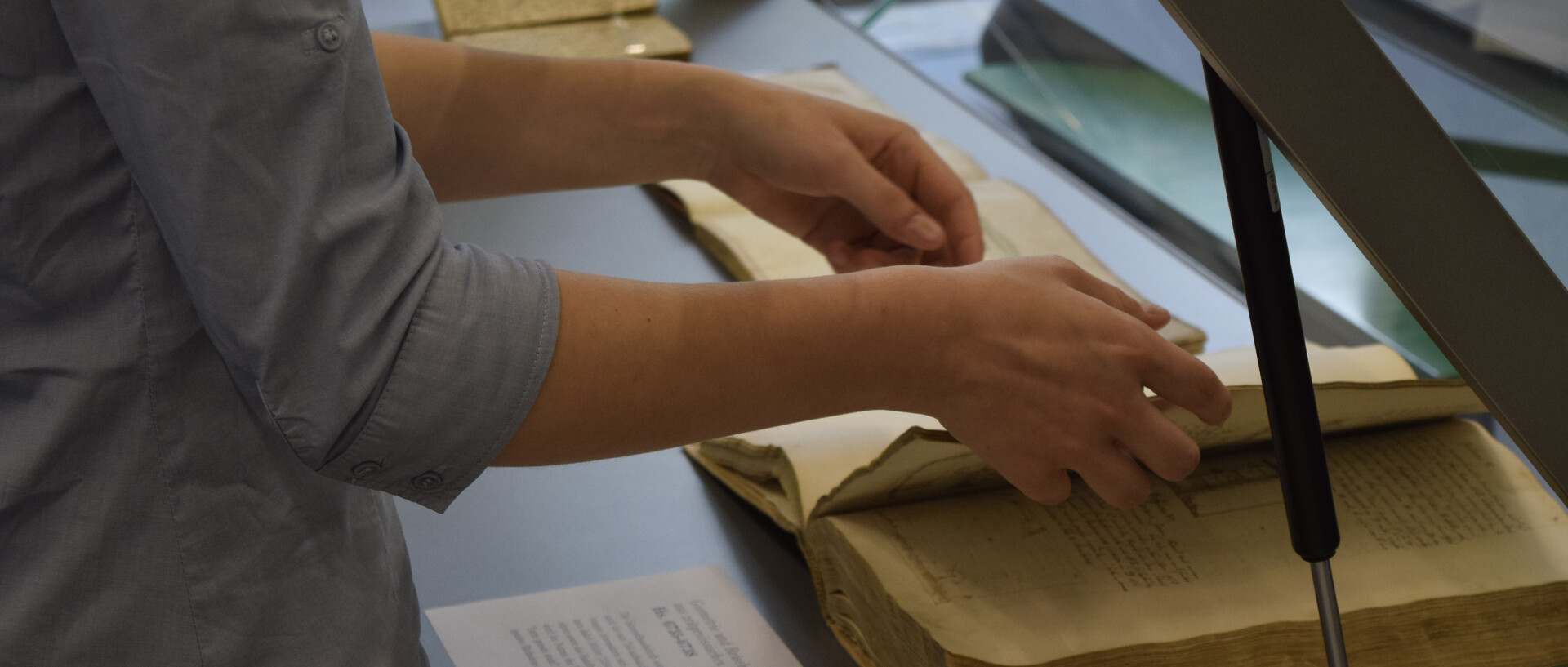 Zwei Hände legen eine Handschrift in eine geöffnete Vitrine