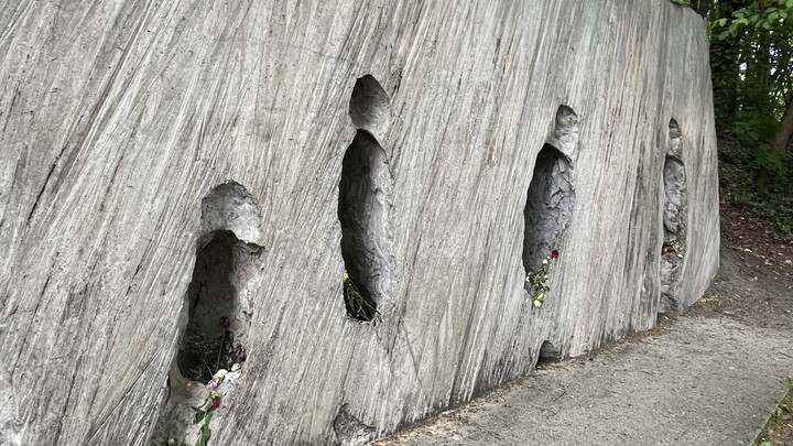 Künstlerische Installation am Mahnmals Gleis 17: Eine lange Betonwand, auf der Negative von Personen zu erkennen sind, die sich Richtung Bahnsteig bewegen.  