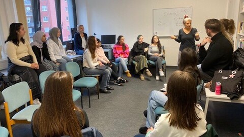 Eine Dozentin steht vor einem Whiteboard und erklärt den Lernstoff, während Schüler*innen und Studierende aufmerksam zuhören.