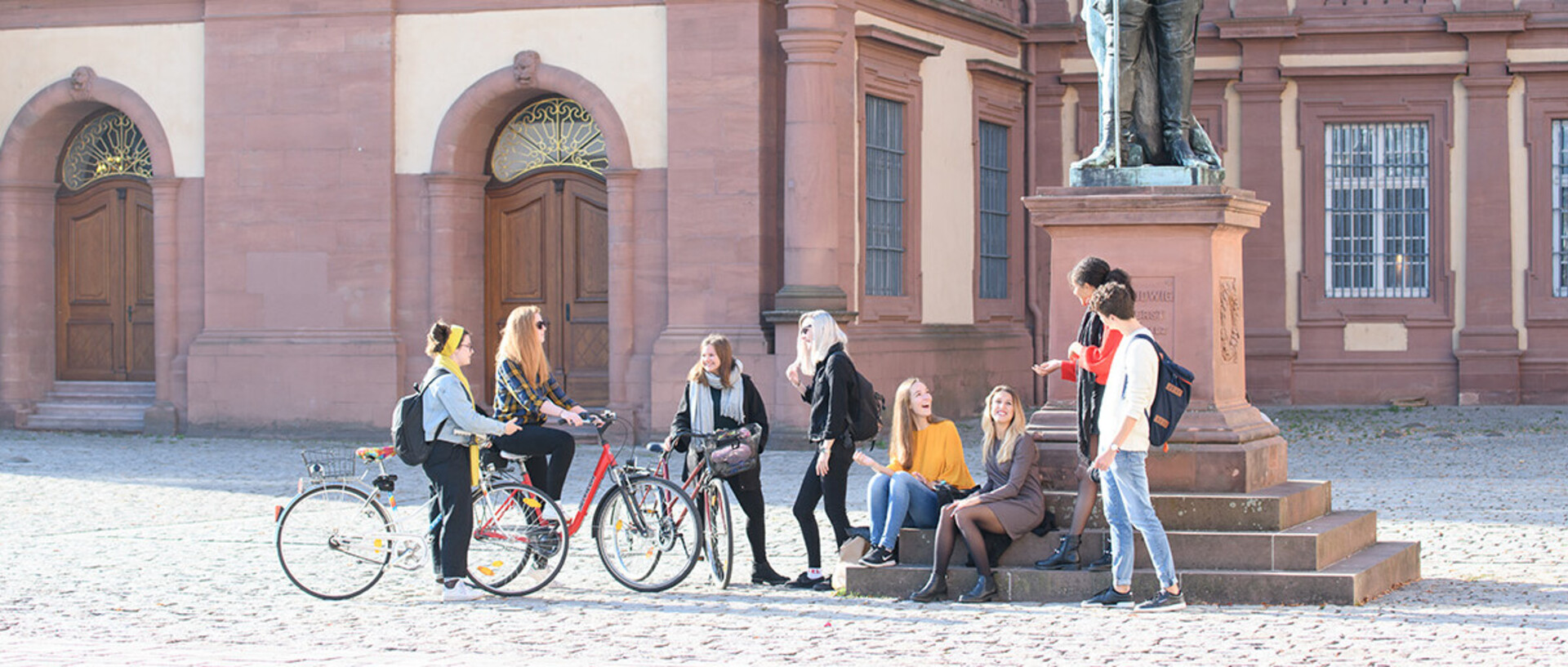Eine Gruppe Studierender steht vor der rechten Statue im Ehrenhof