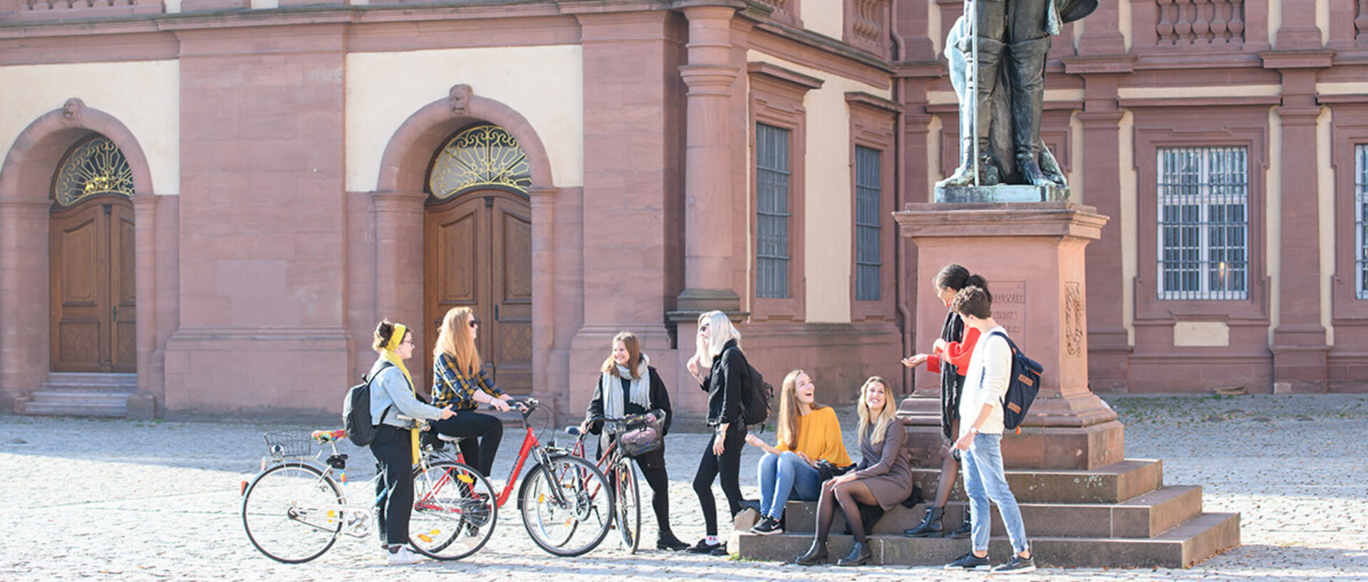 Eine Gruppe Studierender steht vor der rechten Statue im Ehrenhof