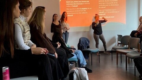 Dozentin erläutert vor der Studierendenpräsentation Eigenheiten der französischen Sprache. Studierende hören zu.rende sitzen im Publikum und folgen aufmerksam der Vorstellung.