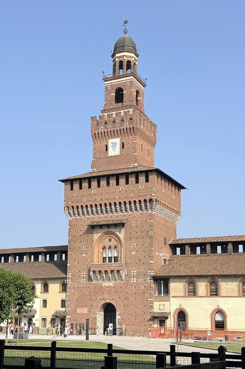 Innenhof des Castello Sforzesco in Mailand mit hohem Turm und Rundturm, davor Bäume und Wiese