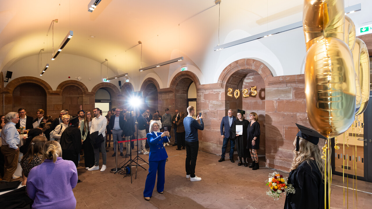 Gäste bei einer Abschlussfeier posieren für Fotos vor goldenen ‘2025’-Ballons.