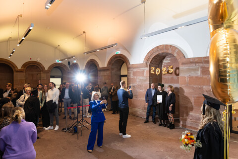 Gäste bei einer Abschlussfeier posieren für Fotos vor goldenen ‘2025’-Ballons.