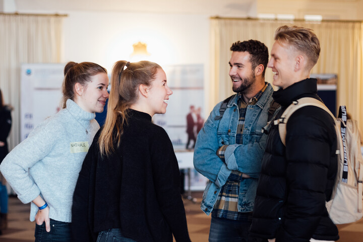 Zwei Studentinnen und zwei Studenten stehen sich gegenüber, unterhalten sich und lachen