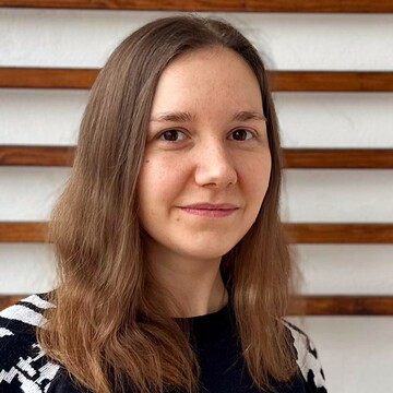 Franziska Knebel trägt einen schwarzen Pullover mit weißem Muster auf den Ärmeln. Sie hat braune Haare und lächelt. 