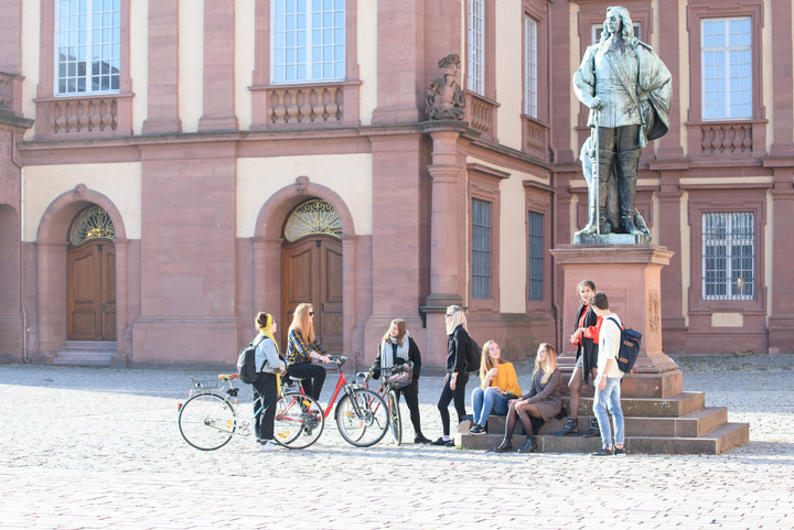 Eine Gruppe aus Studierenden versammelt sich um das Karl-Ludwig-Denkmal vor dem Schloss.