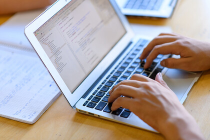 Studierende Person tippt nutzt einen Laptop.