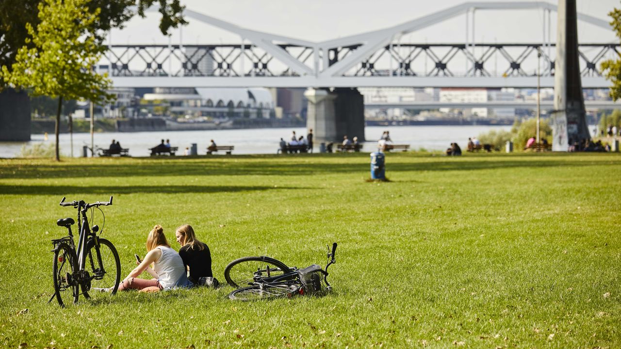 Zwei Frauen sitzen auf einer grünen Wiese am Fluss.