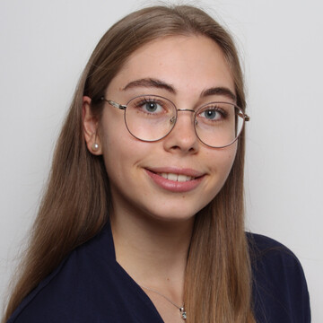Sandra Scherer trägt eine dunkelblaue Bluse und eine silberne Kette. Sie hat braune Haare, trägt eine Brille und lächelt. 