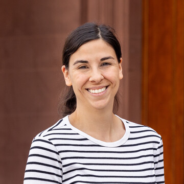Eva Breitbach hat lange, zum Pferdeschwanz zurückgebundene braune Haare und trägt ein weiß-blau gestreiftes Langarmshirt. Sie steht hier lächelnd vor dem Mannheimer Schloss.