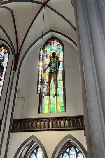 Eines der großen Buntglasfenster in der Nikolaikirche. Darauf abgebildet ist ein schwarzer Mann in bunter Kleidung. Die Fenster sind Teil einer Kunstinstallation. 