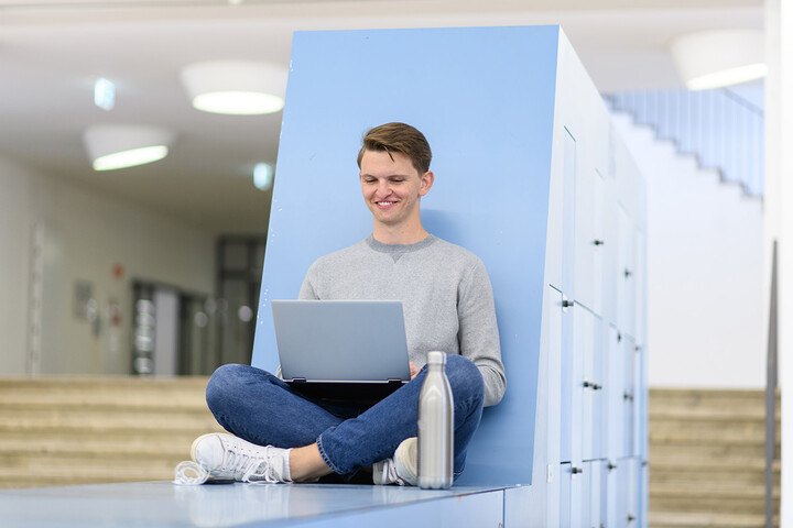 Ein Student sitzt mit seinem Laptop in einem Aufenthaltsbereich der Universität Mannheim.