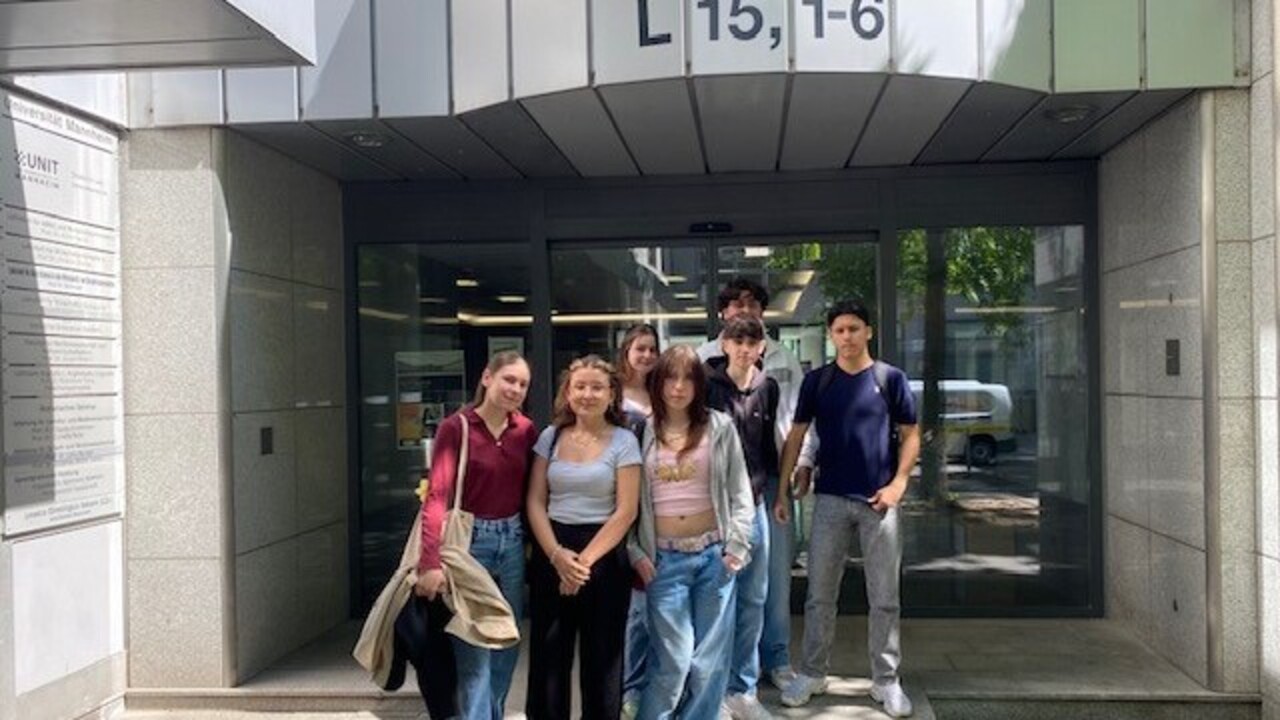 Schüler*innen eines Gymnasiums stehen vor einem Universitätsgebäude in L15, 1-6.