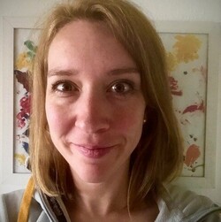 Mareile Rasiller vor einem bunten Gemälde. Sie hat schulterlanges blondes Haar und lächelt. 