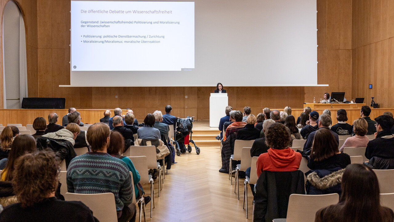 Blick aus dem Mittelgang im Publikum auf die Bühne Welttag der Philosophie 2025: Blick aus dem Mittelgang zwischen dem Stuhlreihen mit Publikum auf die Bühne beim Vortrag von Prof. Dr. phil. Elif Özmen in der Aula der Universität Mannheim mit ihrer Holzvertäfelung bei abgesenkter Leinwand mit darauf projizierter Vortragspräsentation.
