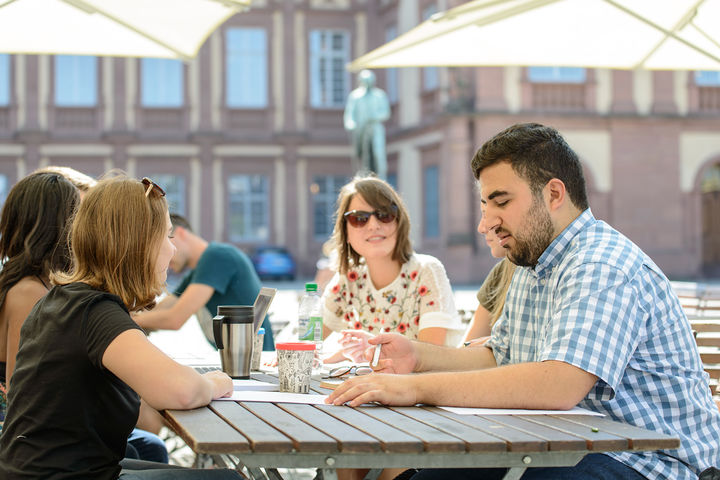 Studierende im Sommer am Tisch vor dem Mannheimer Schloss.